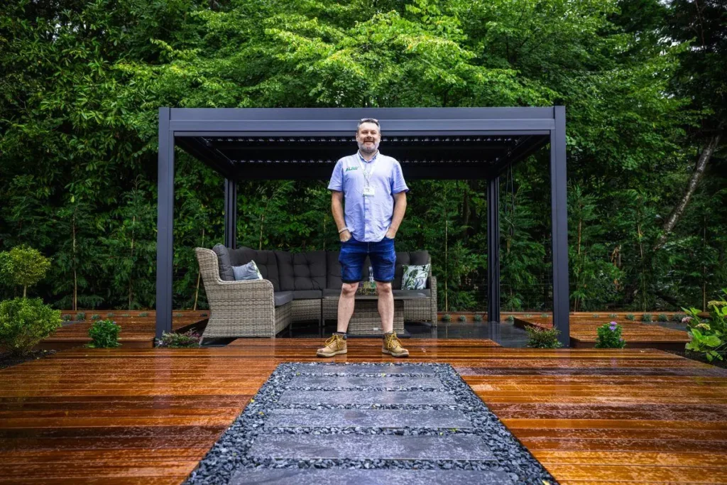 Owen Marsh standing on hardwood decking in front of a dark louvred pergola