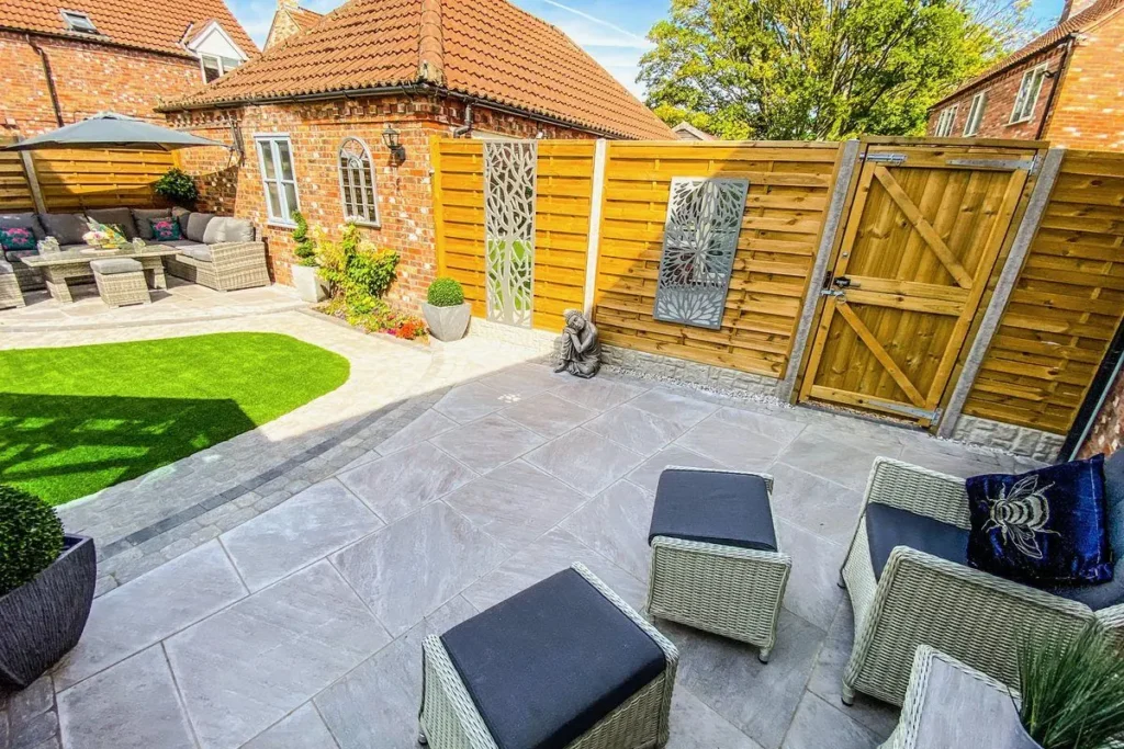 Grey porcelain patio with rattan seating, artificial grass and a timber fence