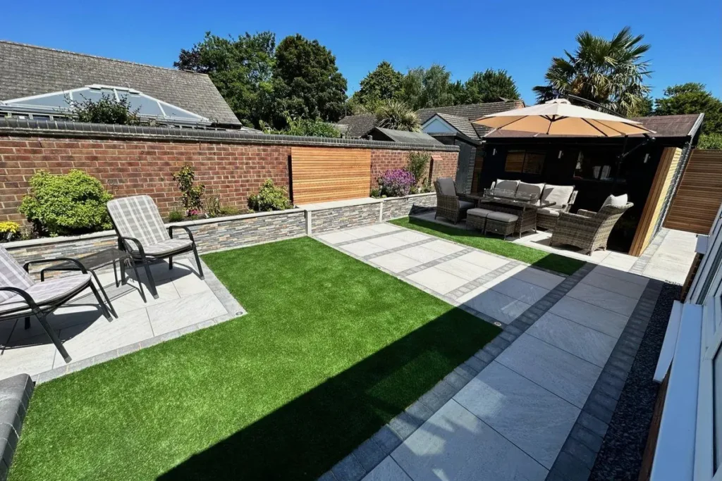 Artificial grass courtyard with porcelain bands, recliners and stone-clad raised beds