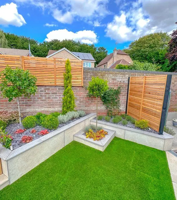 Artificial lawn in front of curved rendered raised beds with shrubs and lollipop trees