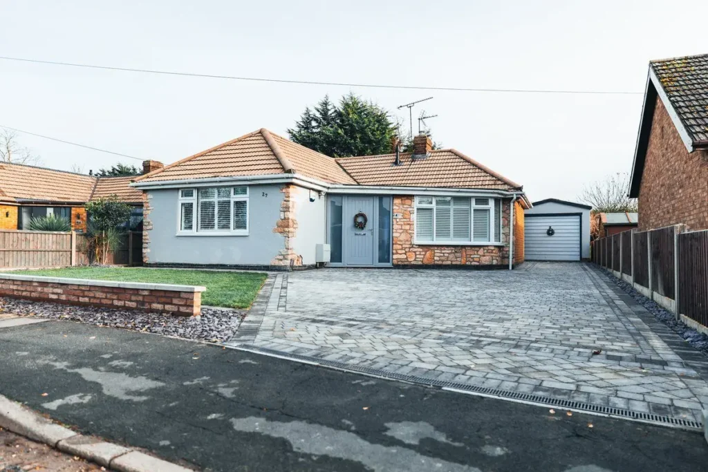 Grey tumbled block-paved driveway with charcoal border and linear drain in front of a rendered bungalow