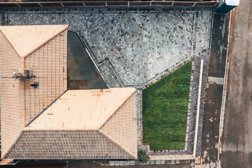 Top-down view of an L-shaped grey block-paved driveway beside a bungalow