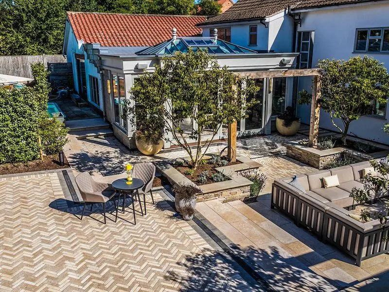 Herringbone paving and light sandstone terrace with outdoor sofa, dry-stone raised beds and oak pergolas