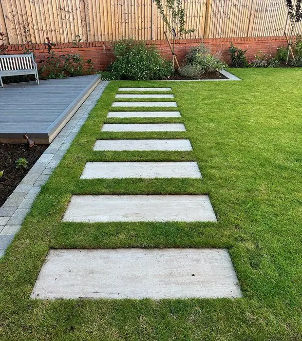 Rectangular stone-effect stepping stones across a lawn to a grey composite deck with a white bench