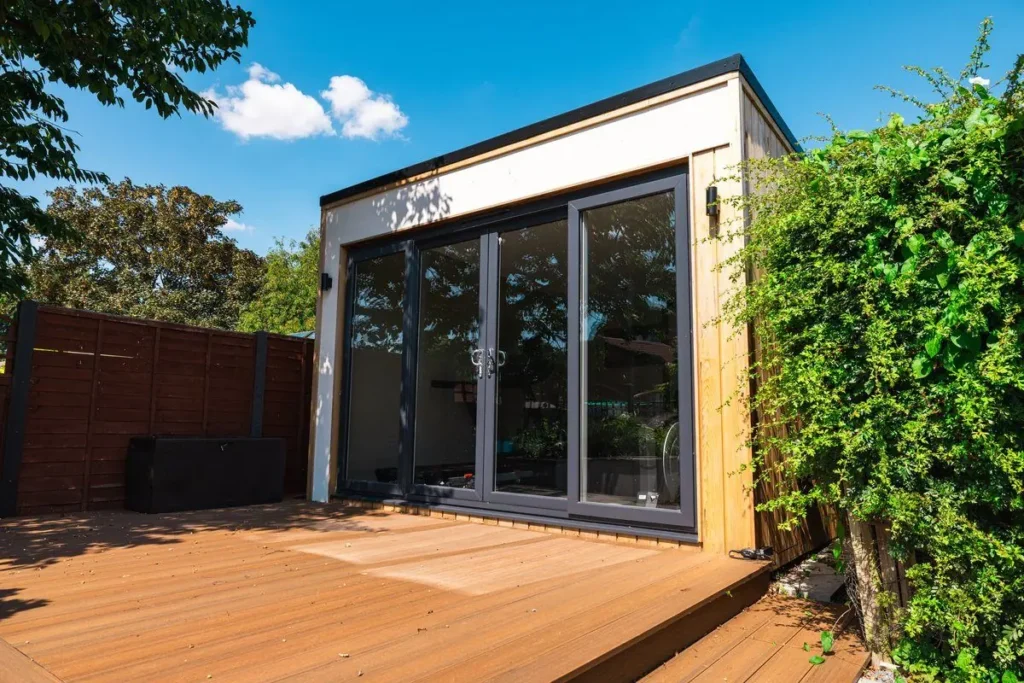White and timber-clad garden room with bi-fold doors on brown composite decking