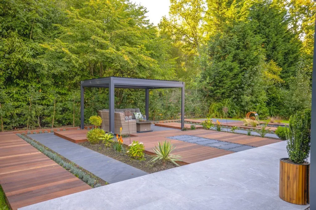 Pale paved path and hardwood deck strips leading to a dark louvred pergola