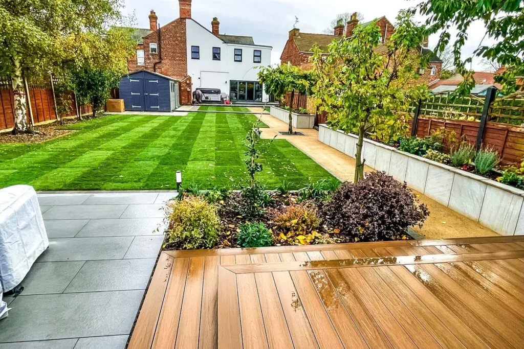 Wet composite decking and grey porcelain patio by an autumn planting bed