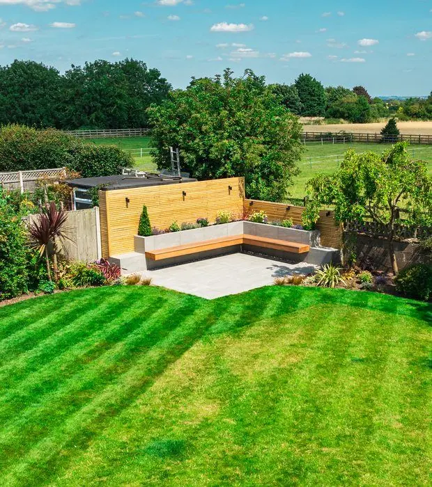 High view over a striped lawn to a slatted timber screen and porcelain patio with a bench