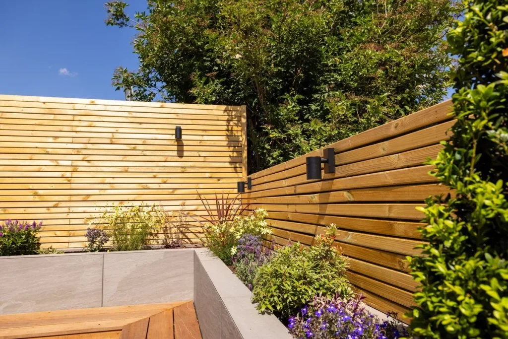 Corner of a horizontal slatted timber screen fence with black wall lights