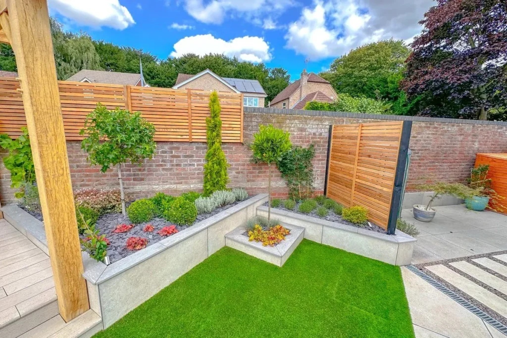 Artificial lawn in front of curved rendered raised beds with shrubs and lollipop trees