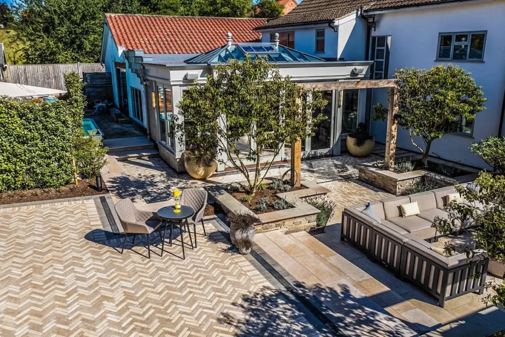Courtyard with herringbone paving, a sandstone terrace, outdoor sofa and raised beds with trees