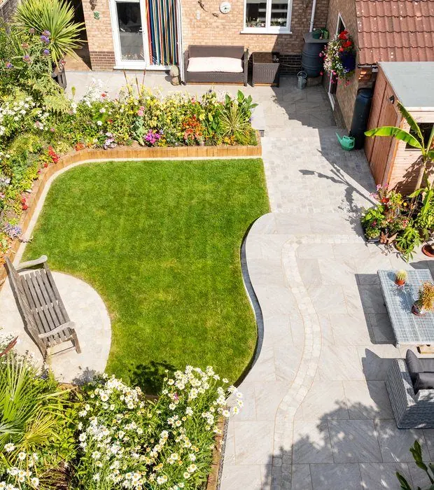 High view of a curved lawn with sleeper edging, a bench on a round pad and a grey paved path to the patio