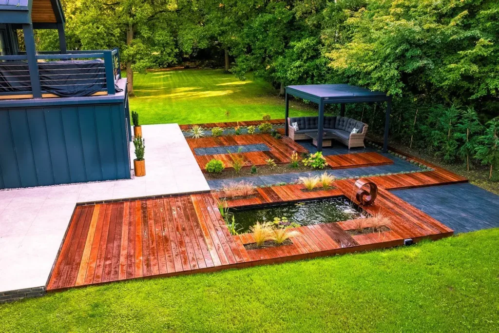 Hardwood decking around a rectangular pond with stepping slabs, planting strips and a louvred pergola