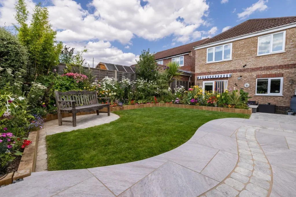 Curved light grey paved path with an inset sett band around a lawn and a bench on a round pad
