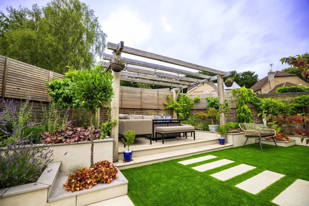 Oak pergola over a sofa platform with stepping stones across an artificial lawn