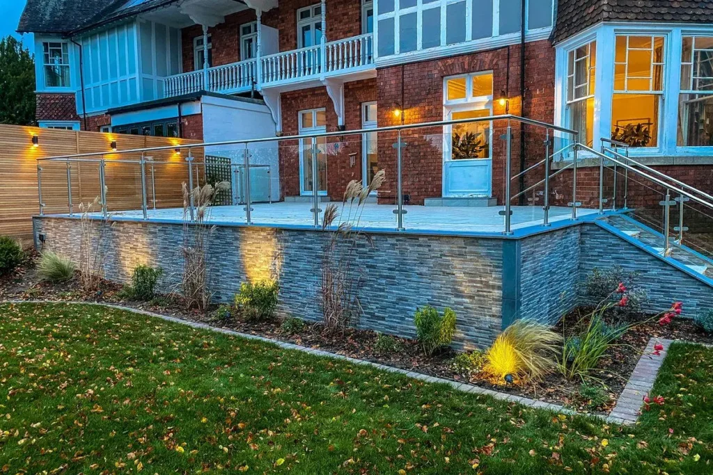 Long raised terrace with grey stone cladding uplit by warm garden lights at dusk