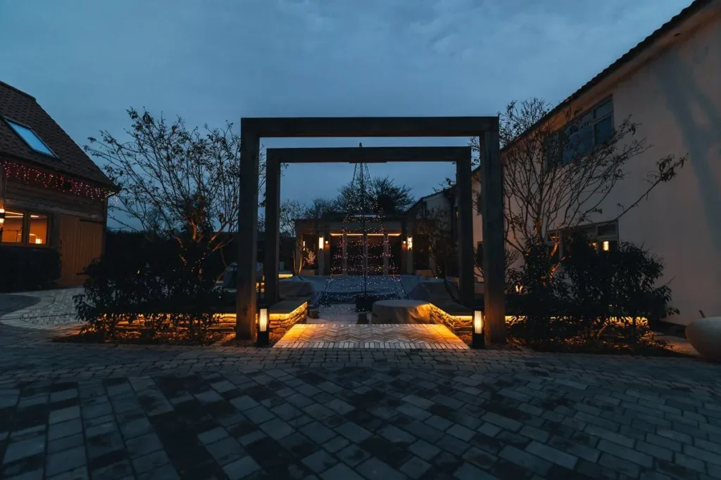 Dark timber pergola frame with bollard lights leading to a lit seating area at dusk