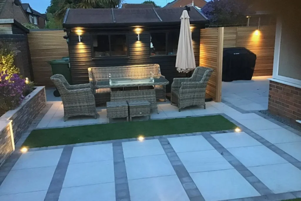 Black shed with wall lights and porcelain paving bands with inset deck lights at dusk