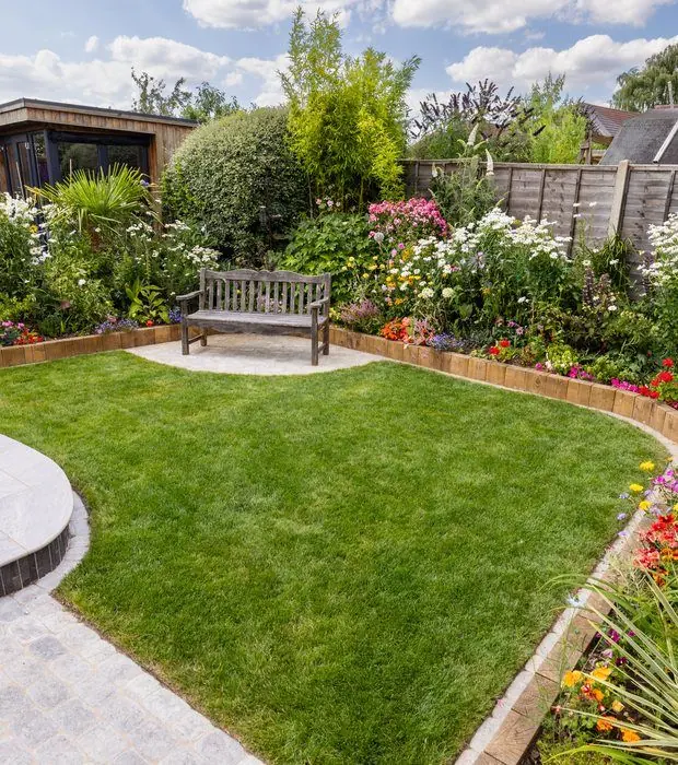 Shaped lawn wrapped by a curved light porcelain path, colourful flower borders and a timber bench
