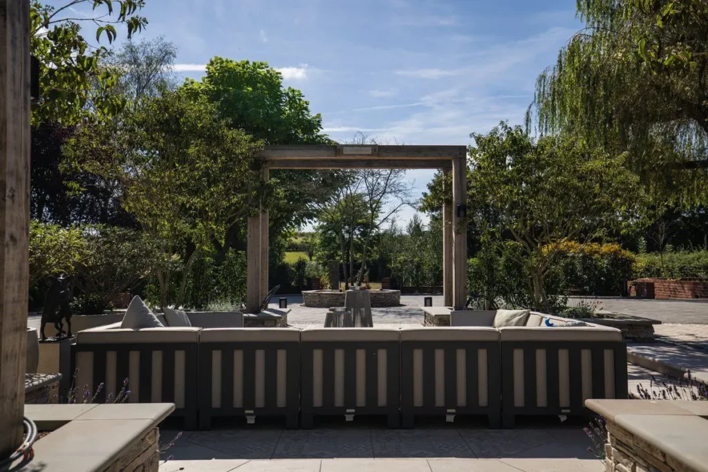 Large slatted outdoor sofa on pale stone paving facing a reclaimed oak arch