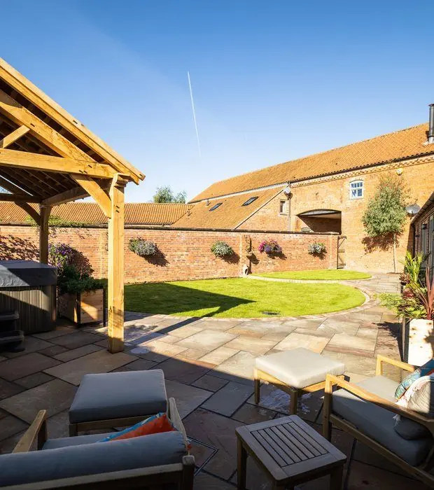 Sandstone patio with cushioned armchairs, an oak-framed gazebo, curved lawn and brick walls