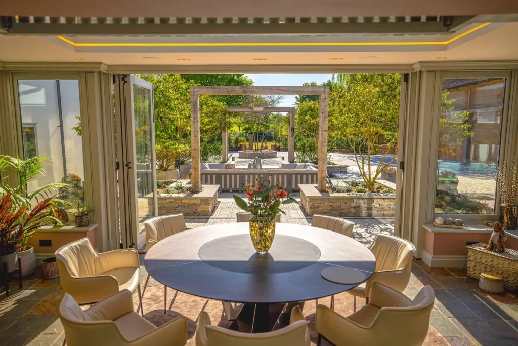 Garden room with round dining table looking out through open bi-folds to oak pergolas