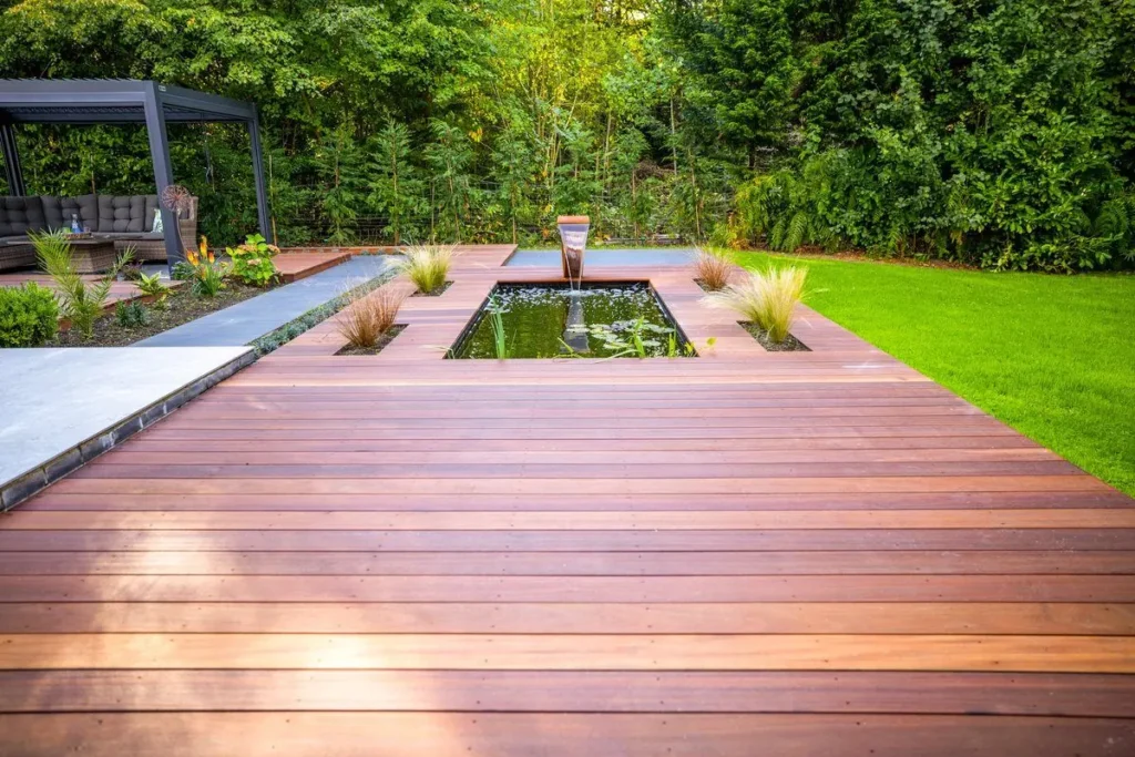Hardwood decking leading to a rectangular pond, with a pergola and lawn beyond