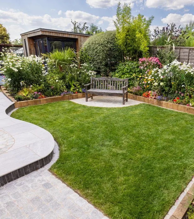 Curved light porcelain path with a dark-edged step around a shaped lawn, flower borders and a timber bench