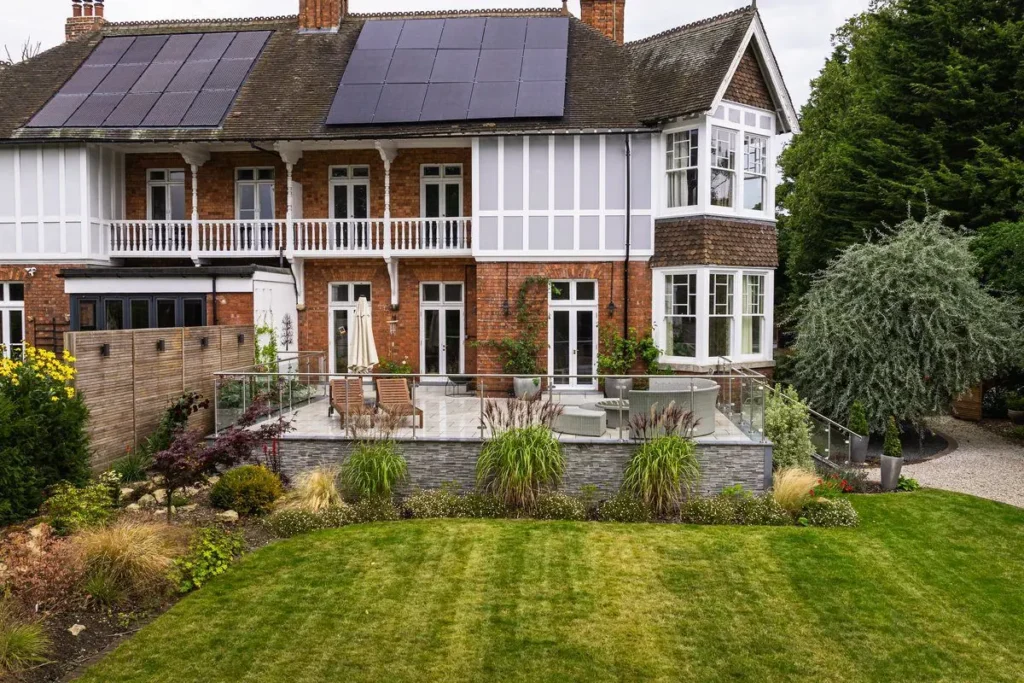 Striped lawn and planted borders in front of a raised porcelain patio and a period house