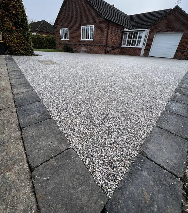 Silver-white resin-bound drive framed by charcoal block edging leading to a red-brick bungalow